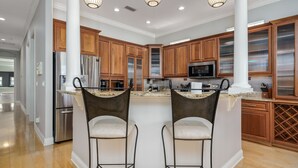 A modern kitchen with wooden cabinets, stainless steel appliances, and a central island with bar stools. - Beach Haven Private Heated Dip Pool! (Palm Coast)