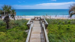 A wooden boardwalk leading to a beach with clear blue water and a palm tree on the left. - Beach Haven Private Heated Dip Pool! (Palm Coast)