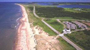 Vue aérienne d’une zone côtière avec une plage, un parking et une route qui serpente à travers le paysage.