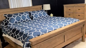 Una camera da letto con un letto di legno, un comodino, una cassettiera e un cartello appeso al muro.
