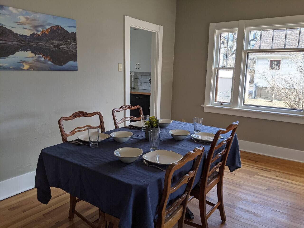 Een eetkamer met een tafel voor vier personen, houten stoelen, een blauwe tafelkleed en een schilderij aan de muur.