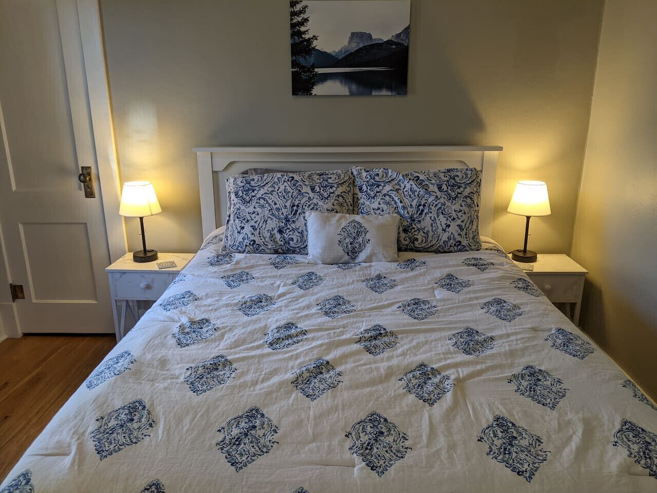 Un lit bien fait, recouvert d’une couvre-lit à motifs et agrémenté d’oreillers assortis, flanqué de deux tables de chevet avec des lampes, dans une pièce au design simple et épuré.