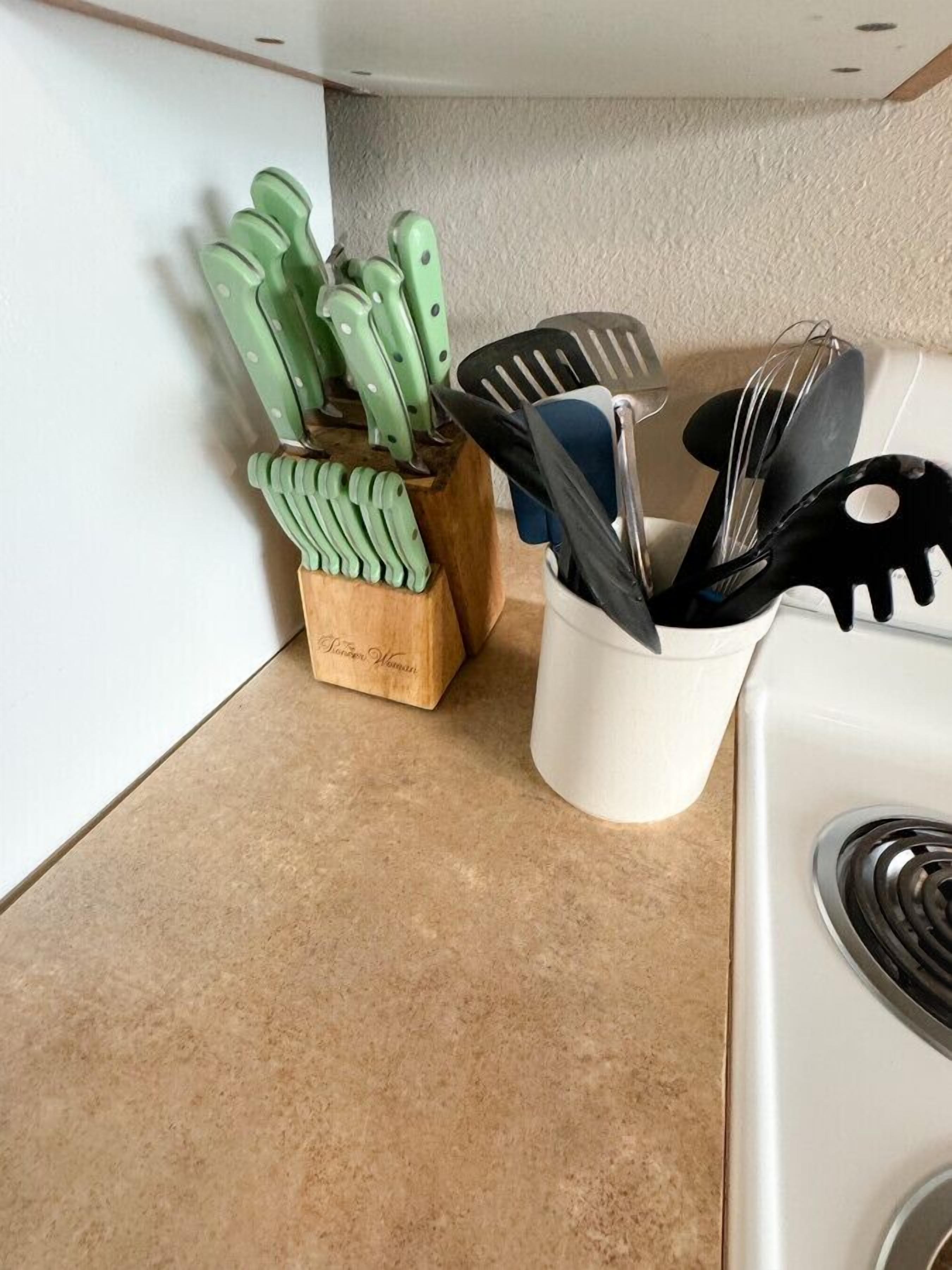 A kitchen counter with a wooden knife block and a white utensil holder.