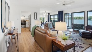 A modern living room with a sofa, a coffee table, and a view of a lake. - Smith Mountain Lake Condo with Main Channel Views (Moneta)