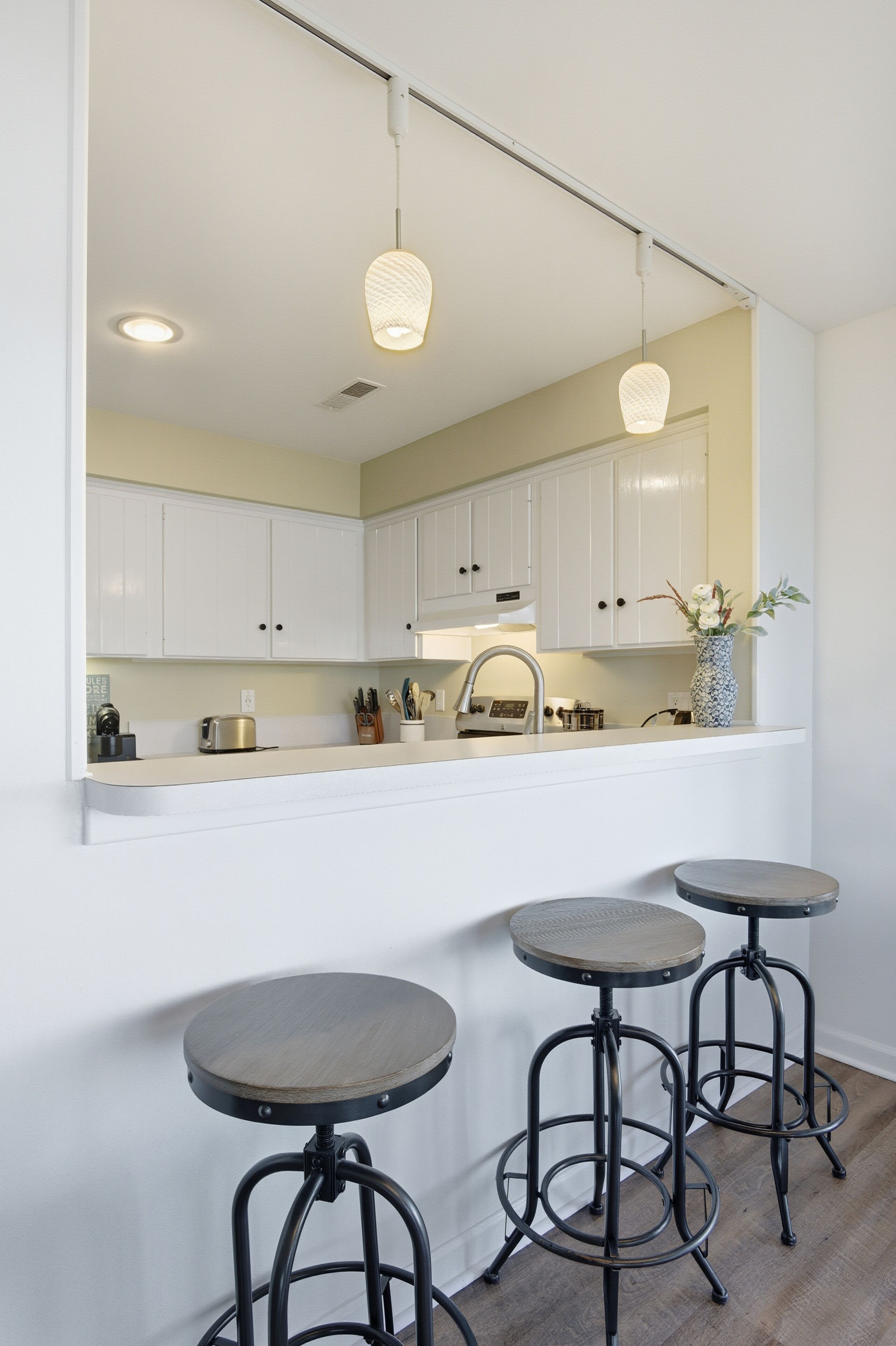 A kitchen with white cabinets, a countertop, a sink, and three stools.