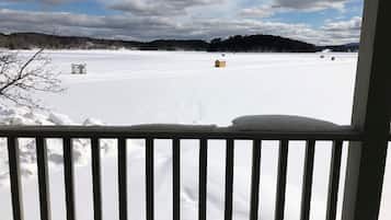 A snowy landscape with a clear sky, a wooden railing in the foreground, and a distant view of trees and buildings.