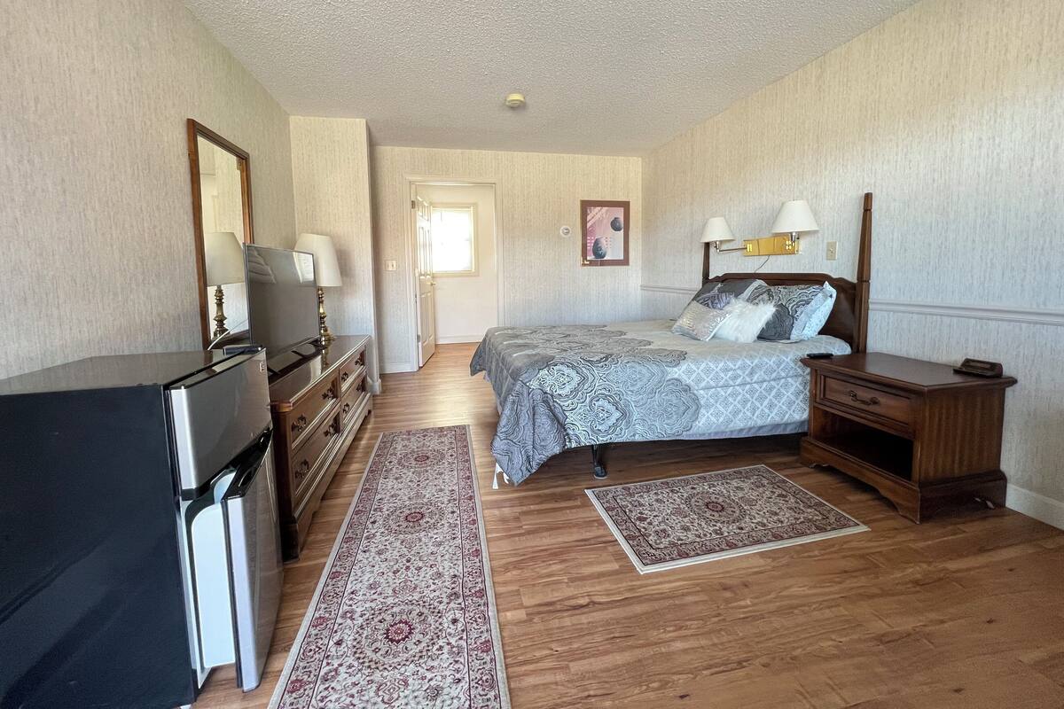 Une chambre à coucher comprenant un lit, une commode, un téléviseur et une porte donnant sur une autre pièce.