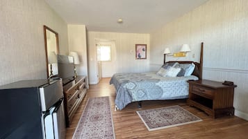 A bedroom with a bed, dresser, TV, and a door leading to another room.