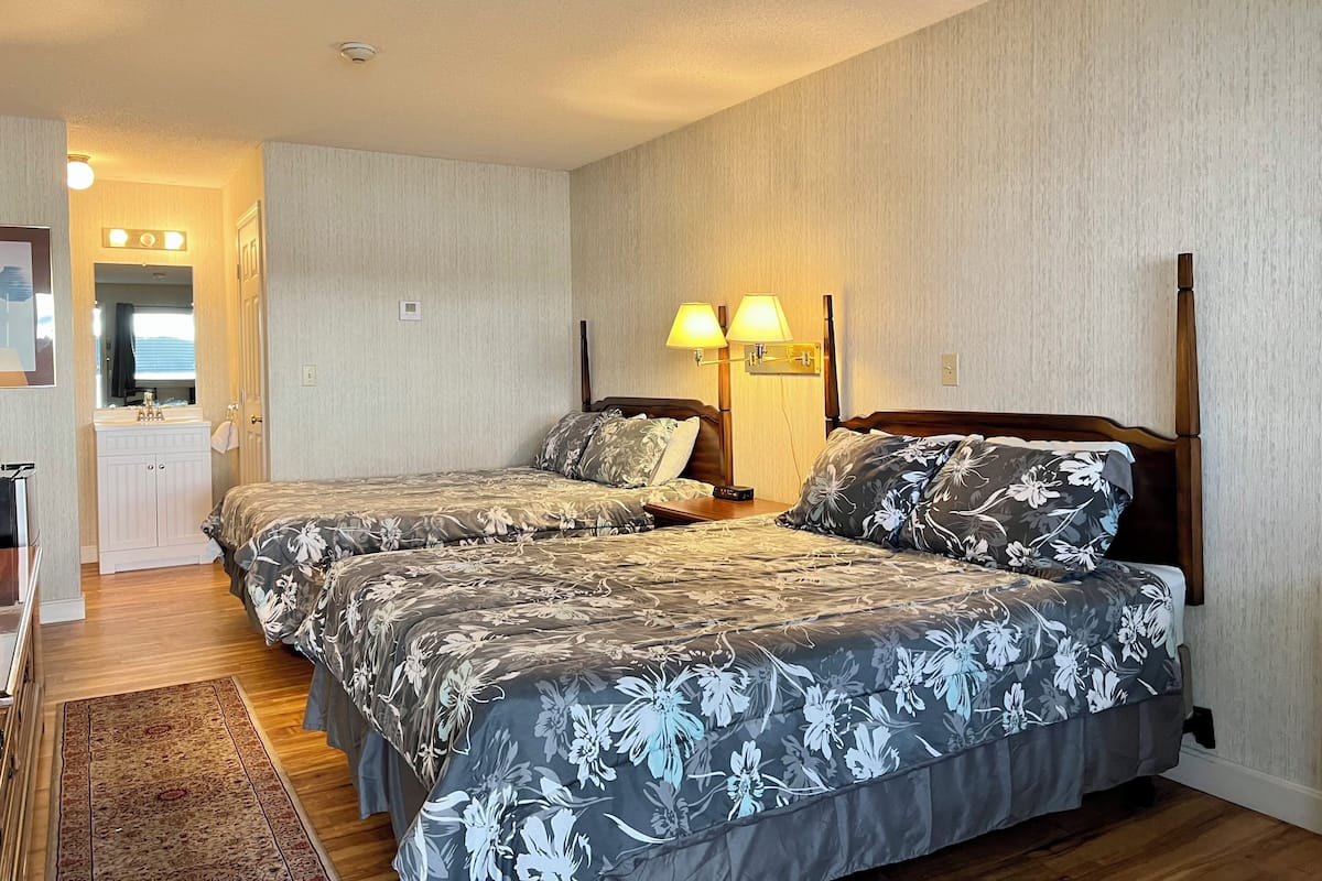 Une chambre d’hôtel avec deux lits, une coiffeuse avec un miroir et une table de chevet avec une lampe.