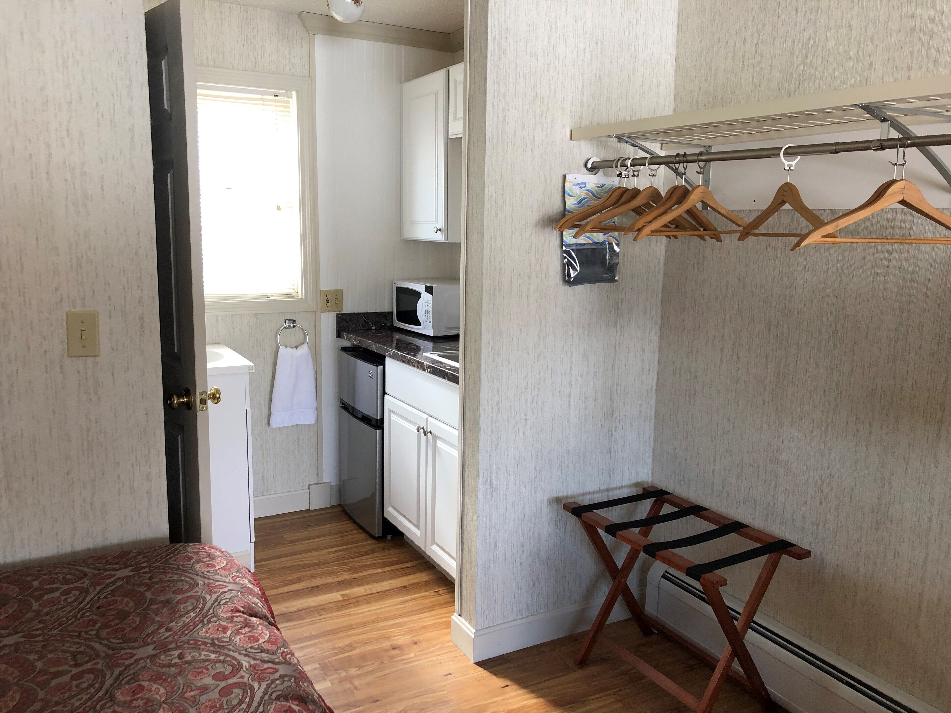 Un dormitorio pequeño con una colcha estampada, un tendedero de madera y una kitchenette con microondas y escurreplatos.