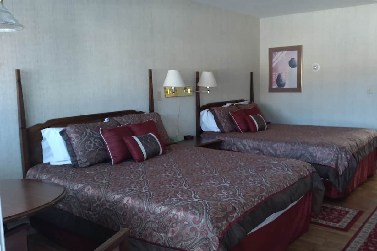 Une chambre d’hôtel avec deux lits, chacun agrémenté de draps et d’oreillers à motifs, une table de chevet, une petite commode, une lampe et un petit bureau avec une chaise.