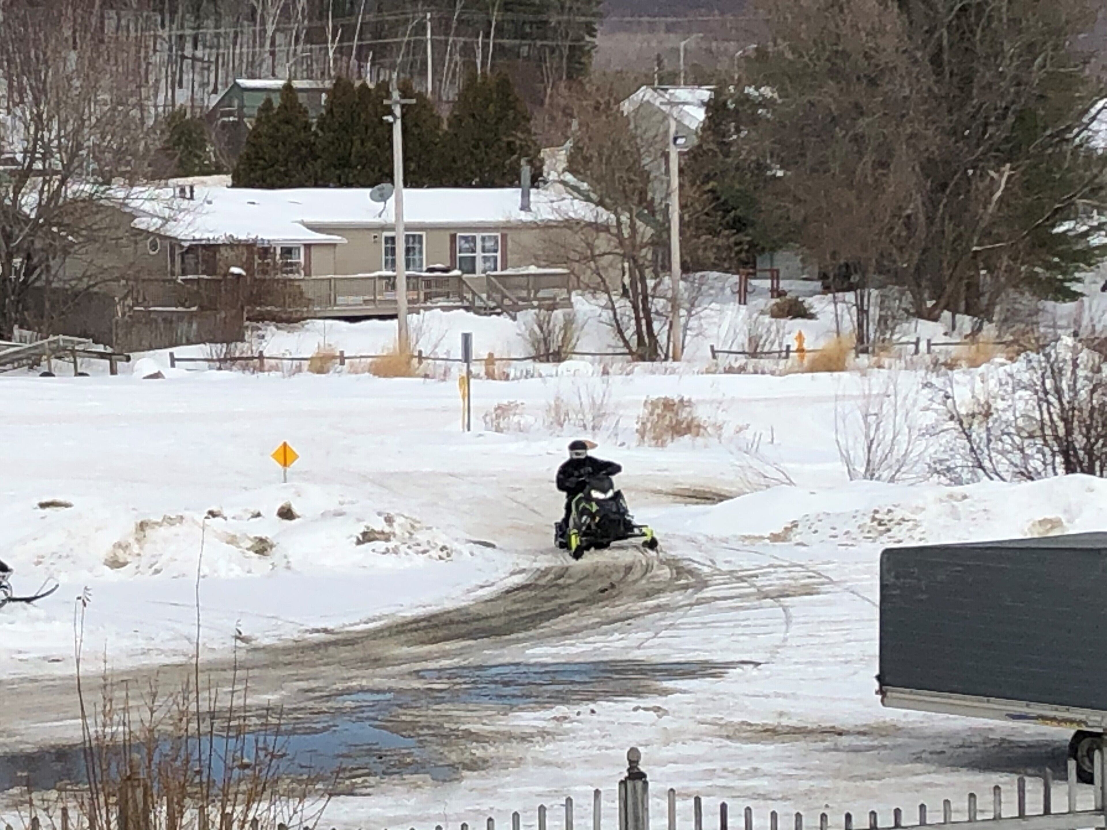 A snow-covered landscape with a person riding a snowmobile on a dirt path.