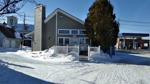 Une maison à deux étages, dotée d’une grande cheminée, d’un porche avec une balustrade blanche et d’une allée recouverte de neige.