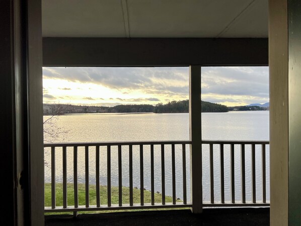 Une vue depuis un balcon doté d’une balustrade, donnant sur une étendue d’eau et une côte lointaine, avec des arbres et des collines.