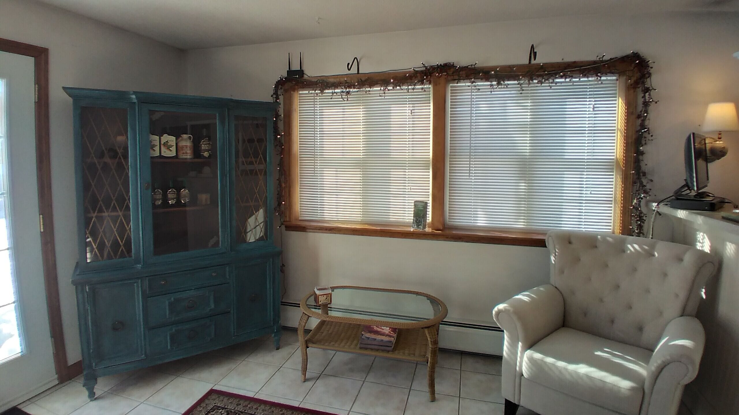 Una sala de estar con un aparador azul, una mesa de centro de vidrio, un sillón blanco y un ventanal con persianas.