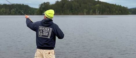 A person fishing by a lake with a forest in the background.