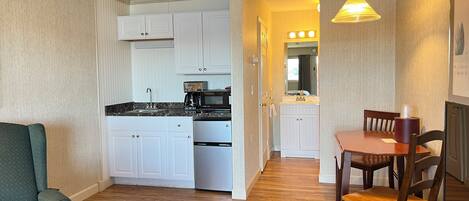 A compact kitchen with white cabinets, a microwave, and a coffee maker. There is a dining table with chairs and a hanging light fixture.