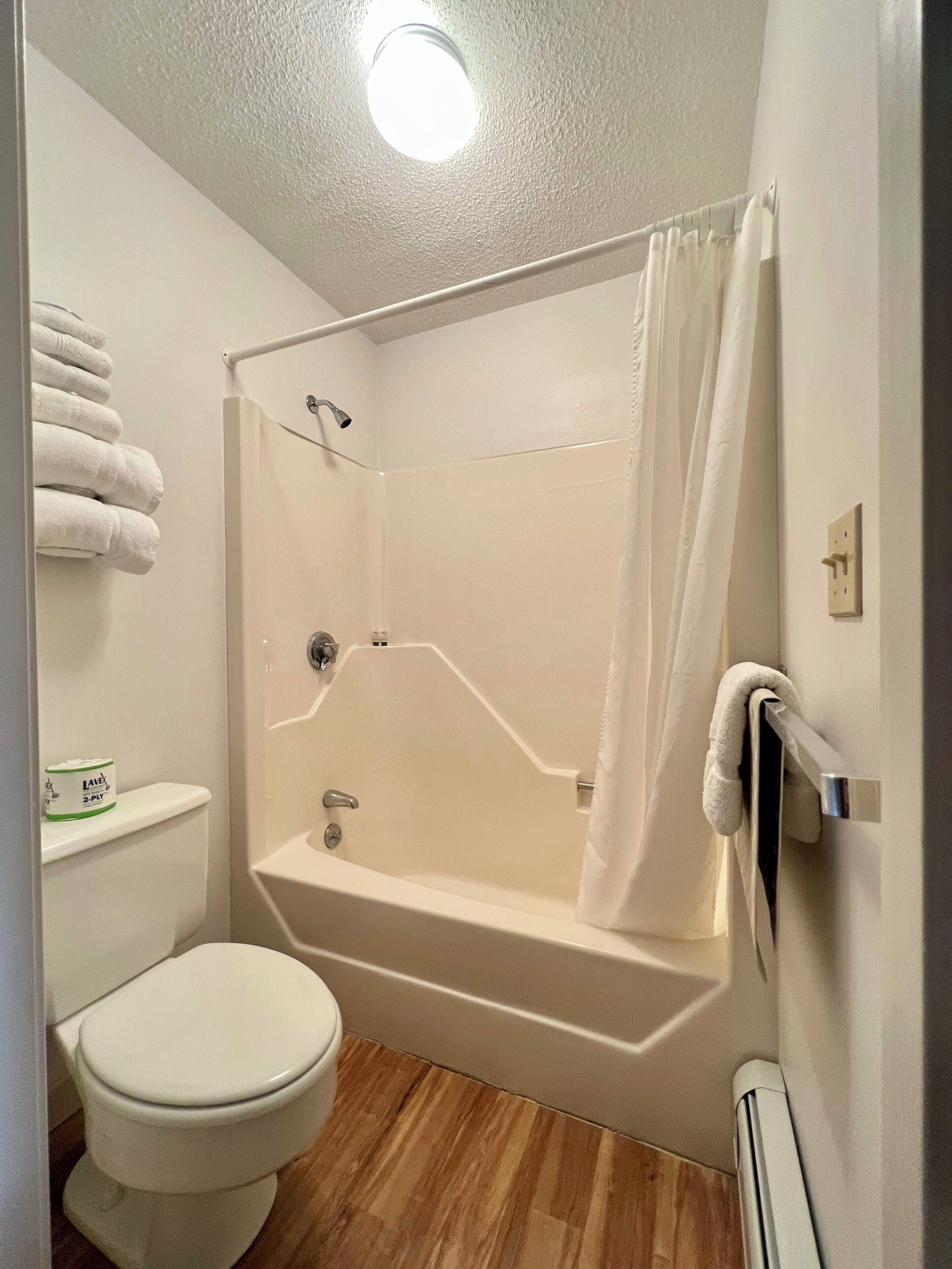 A bathroom with a shower, toilet, and a towel rack with towels.