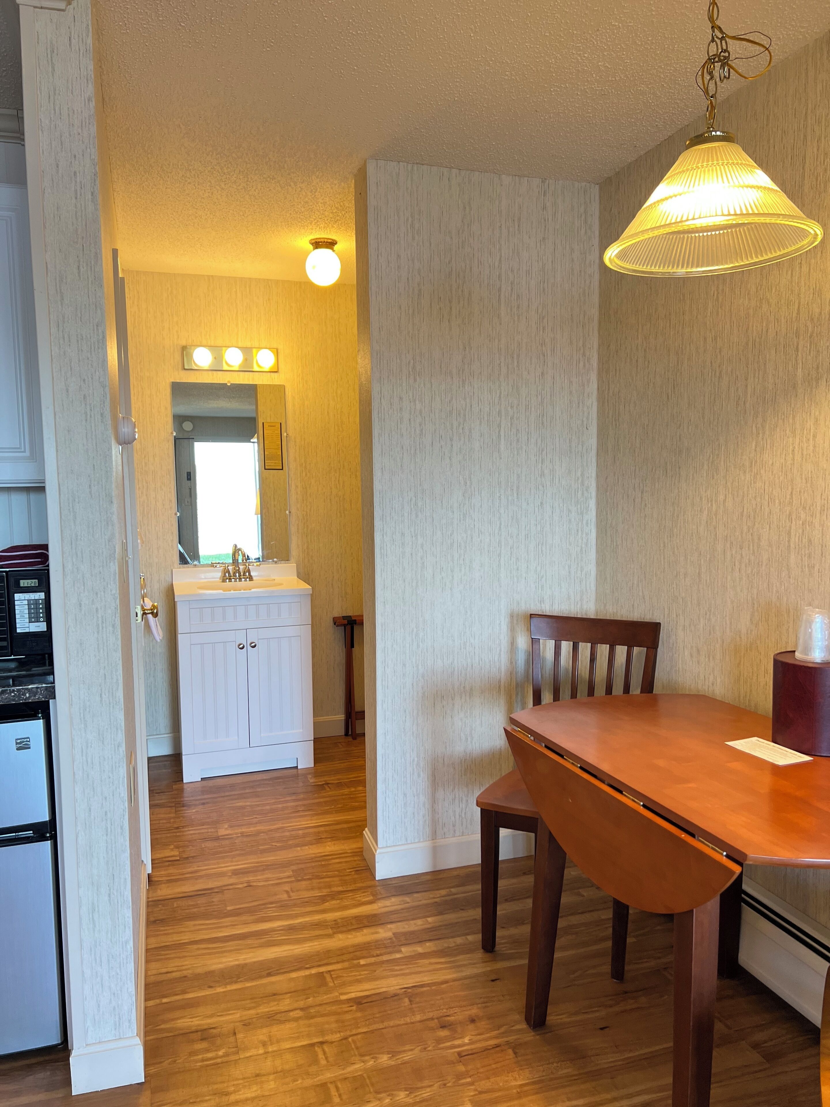 A compact kitchen with a refrigerator, sink, and a wooden dining table with chairs.