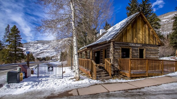 Eine Holzhütte mit Veranda und Treppe, mit dem Schild "Pitkin Creek", umgeben von Schnee und Bäumen.