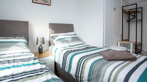 A hotel room with two beds, a bedside table with a lamp, a framed picture on the wall, and a clothing rack. - 2 bedroom accommodation in Kingsbridge (Kingsbridge)