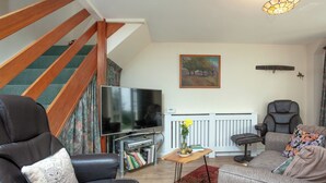 A living room with a sofa, a chair, a television, a small table with a vase and books, and a staircase. - 2 bedroom accommodation in Kingsbridge (Kingsbridge)
