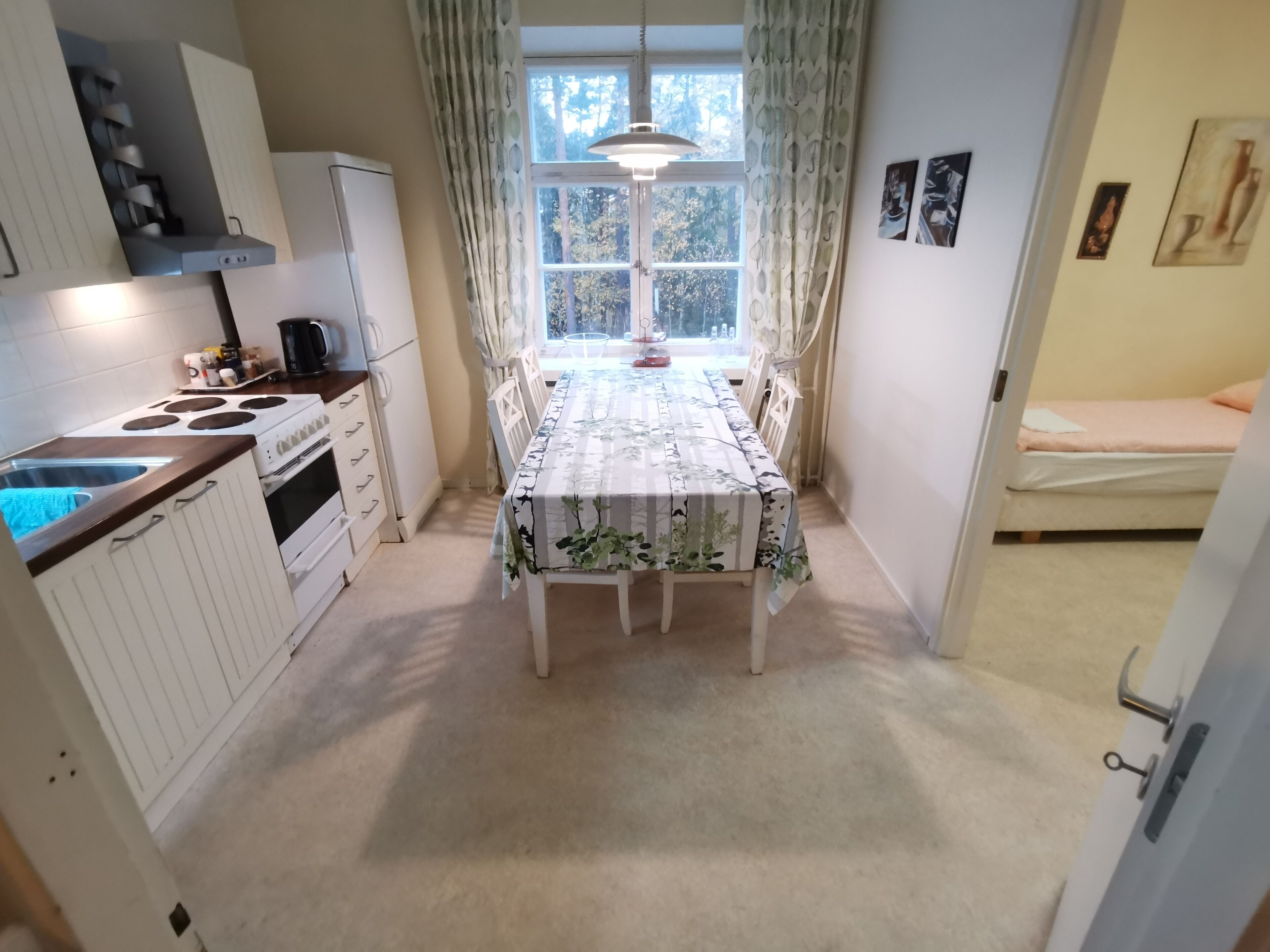 A compact kitchen with white cabinets, a stove, and a dining table with a floral tablecloth.