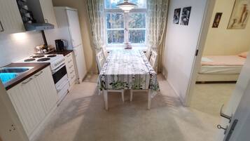 A compact kitchen with white cabinets, a stove, and a dining table with a floral tablecloth.