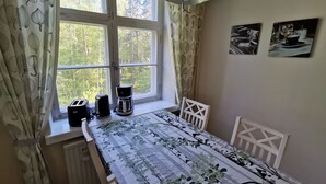 Una habitación con una cama, una mesa con mantel, una cafetera, un tostador y una ventana con cortinas.