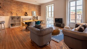 Una sala de estar moderna con pared de ladrillo, piso de madera y un ventanal con vistas a la ciudad.
