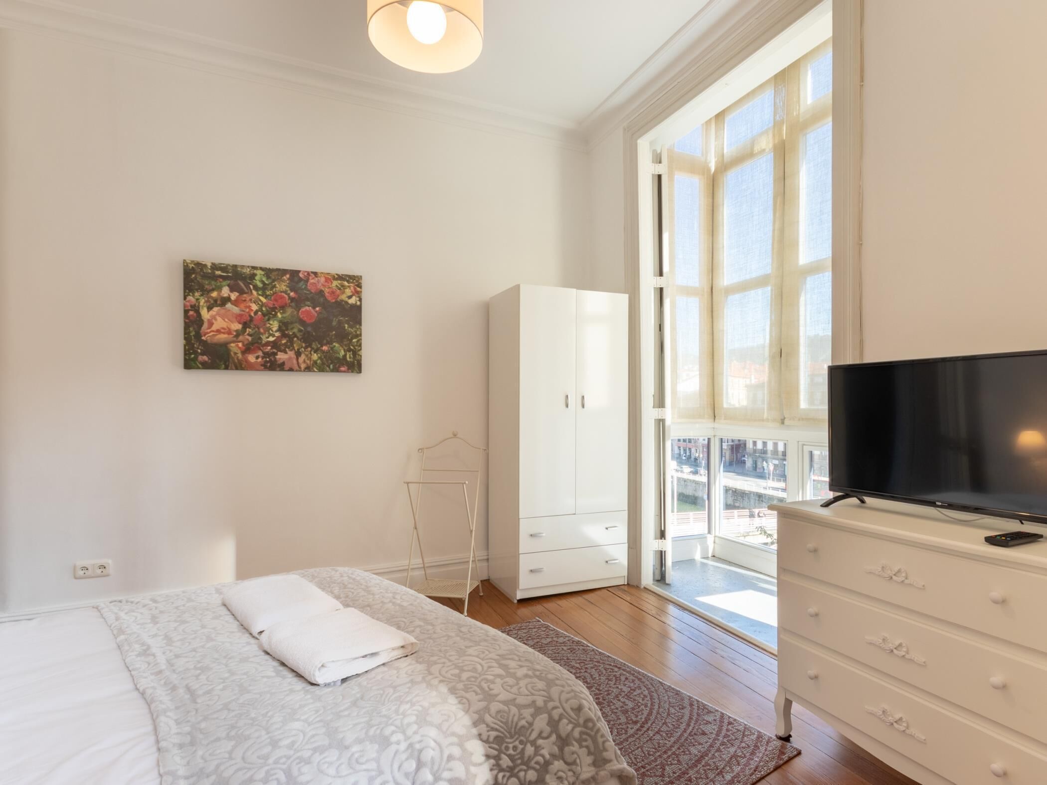 Un dormitorio con cama, televisor, armario y ventana con vistas.