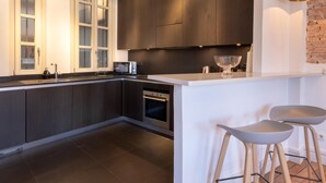 Una cocina moderna con armarios oscuros, encimera blanca y horno integrado. Hay dos taburetes de bar y un bol de vidrio grande en la isla.