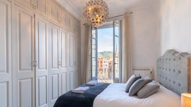 Un dormitorio con una cama grande, vistas de edificios a través de una ventana y una araña.