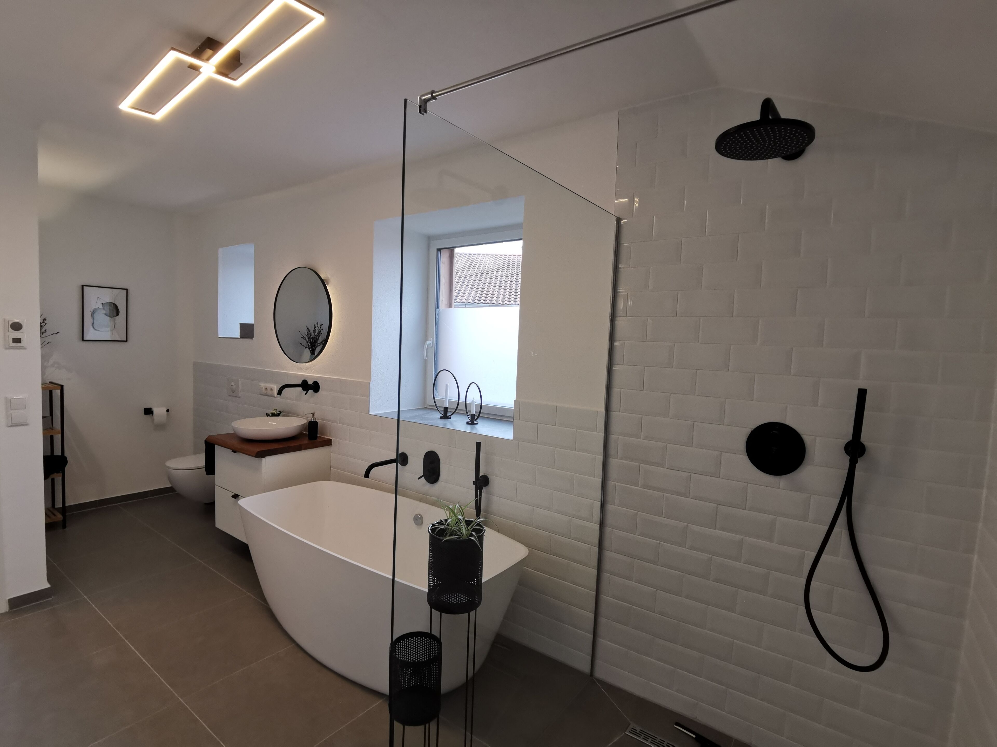 Ein modernes Badezimmer mit einer freistehenden Badewanne, einer Duschkabine aus Glas und einem weiß gefliesten Duschbereich.