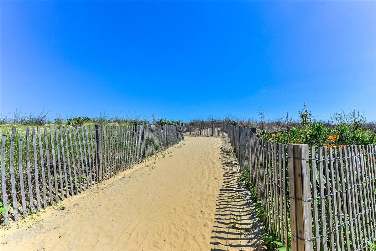 A sandy pathway flanked by wooden fences leading to a distant point.