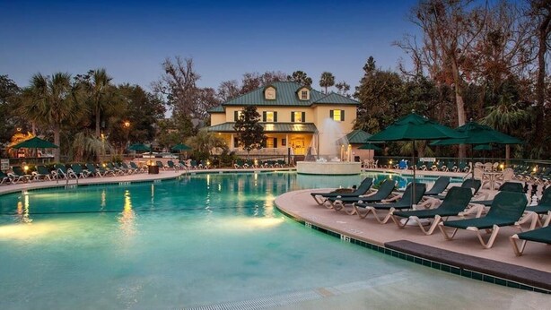 A pool area with lounge chairs and umbrellas, a fountain, and a building in the background. - Hilton Head vacation resort: 2 blocks from the beach, near restaurants and golf! (Hilton Head Island)