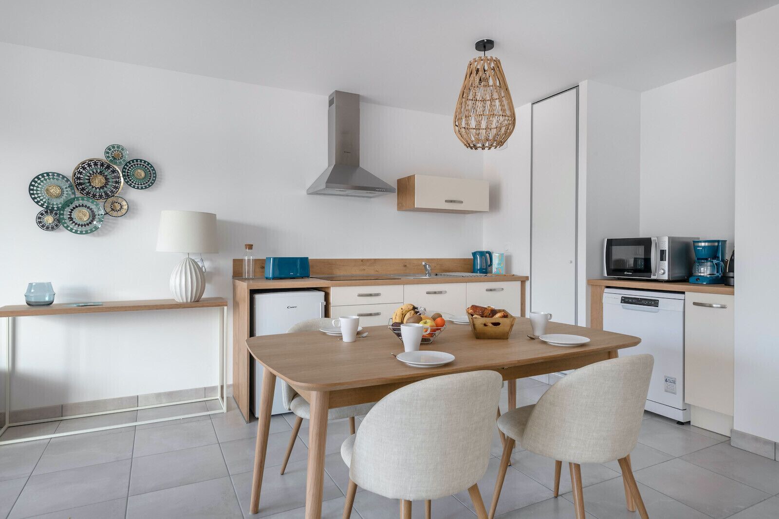 A modern kitchen with a wooden table, four chairs, a built-in oven, a microwave, and a coffee maker.