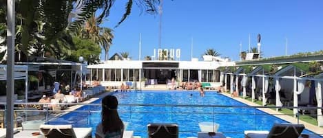 A pool area with lounge chairs, a clear view of the pool, and a building with signage in the background.