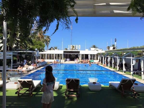A pool area with lounge chairs, a clear view of the pool, and a building with signage in the background.