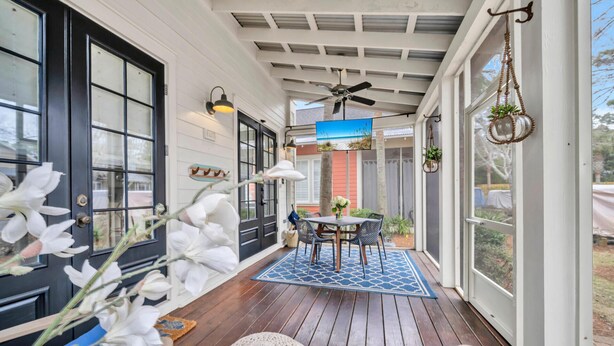 Eine überdachte Veranda mit Holzterrasse, einem Tisch mit Stühlen und einem Deckenventilator.