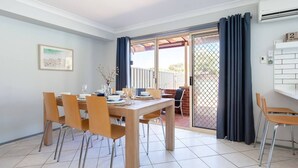 A dining area with a table set for four, chairs, a window with curtains, and a view of the outdoors. - Blue Bay - Close to Fingal Bay Beach. Mid Week Stay Special Now On. (Fingal Bay)