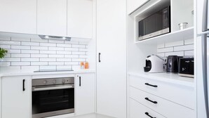 A modern kitchen with white cabinetry, a built-in oven, a microwave, and a coffee maker. - Blue Bay - Close to Fingal Bay Beach. Mid Week Stay Special Now On. (Fingal Bay)