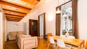 Una habitación acogedora con techo de madera, un sofá, una mesa de comedor con sillas y una ventana con cortinas.