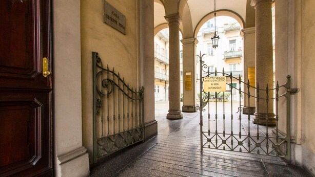 Un pasillo con puerta de madera, rejas metálicas y un cartel que indica acceso vehicular restringido.