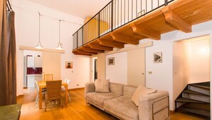 Una sala de estar con sofá, mesa de comedor, sillas y una escalera.