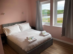 Una cama bien hecha con almohadas y toallas, una ventana con cortinas, y vistas a un paisaje.