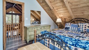 A bedroom with a sloped ceiling, a wooden bed frame, a green dresser, and a large mirror. - Fishin' Bear - Enjoy Spring and Summer in the Smokies! (Sevierville)