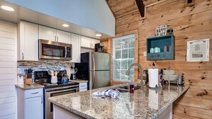 A modern kitchen with granite countertops, stainless steel appliances, and wooden paneling. - Fishin' Bear - Enjoy Spring and Summer in the Smokies! (Sevierville)