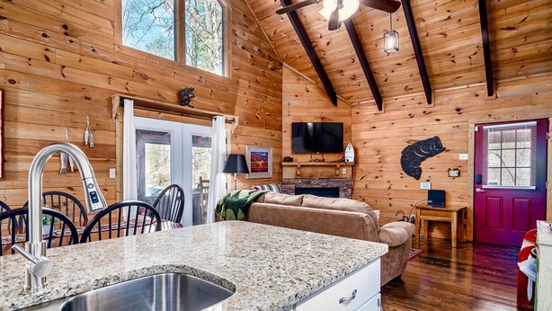 A wooden cabin interior with a kitchen area featuring granite countertops, a sink, and a dining table with chairs. - Fishin' Bear - Enjoy Spring and Summer in the Smokies! (Sevierville)