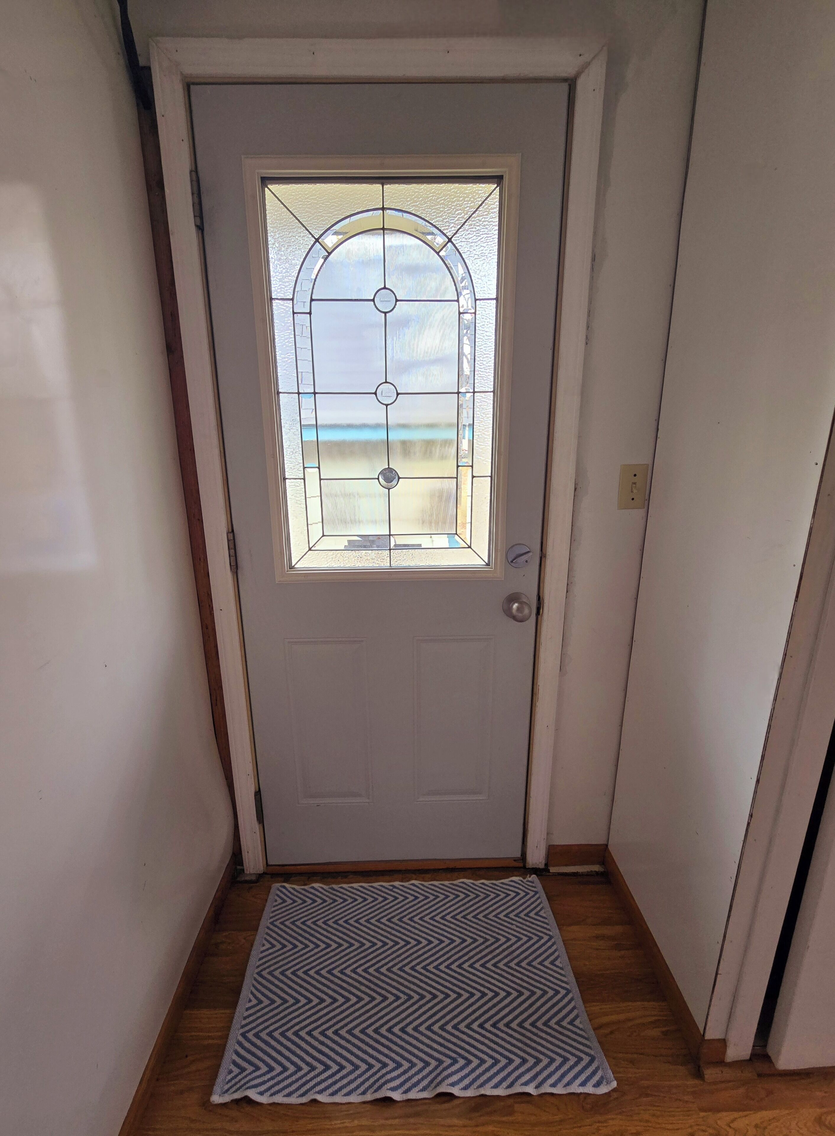 En vit dörr med en glasruta och ett handtag av metall.